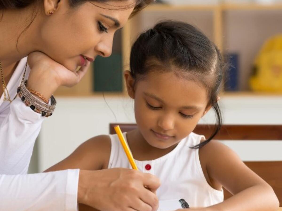 A woman assists a girl of about five with writing 
